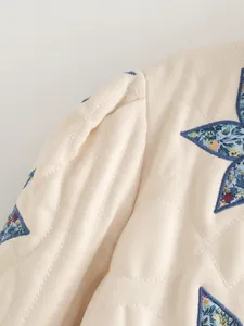 Dettaglio giacca trapuntata beige con patchwork di stelle floreali e maniche a sbuffo.