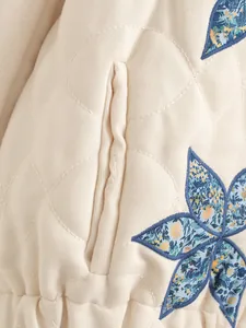 Dettaglio ricamo floreale e tasca su giacca trapuntata color crema in stile francese