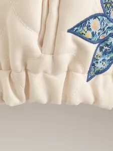 Dettaglio del bordo della giacca trapuntata con vita elastica e toppa a fiori blu