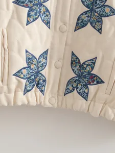 Dettaglio della giacca trapuntata beige con applicazioni floreali e bottoni in tessuto