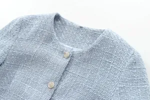 Close-up detail of a light blue round neck tweed jacket with golden crest buttons