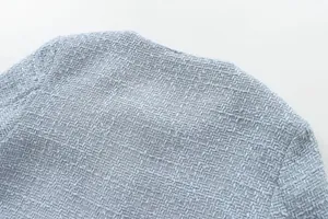 Macro view showing the intricate light blue tweed weave on women's cropped jacket