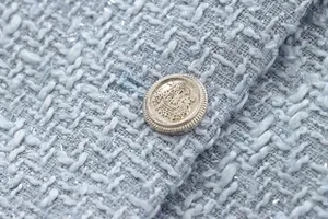 Close-up detail of light blue tweed bouclé fabric texture and an ornate silver metal button