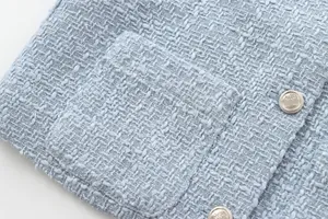 Close-up detail of light blue tweed jacket featuring crest buttons and pocket texture.