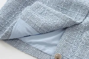 Close-up of light blue tweed jacket showing textured fabric, inner lining and crest button.