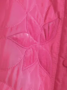 Dettaglio macro del ricamo floreale rosa su una giacca trapuntata in stile francese.