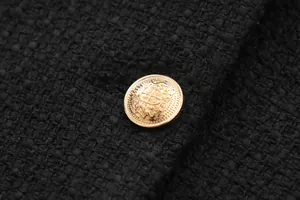 Detailed macro view of a vintage embossed gold button on a black Chanel style tweed jacket