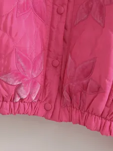 Dettaglio ravvicinato della giacca rosa con applicazioni in velluto a foglia e bottoni