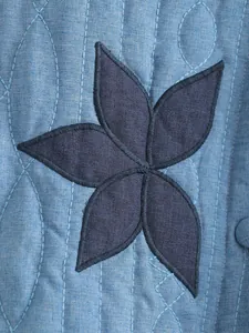 Dettaglio macro dell'applique floreale e della trama trapuntata della giacca blu