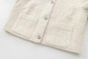 Close-up of cream tweed jacket showing textured fabric and silver embossed buttons.