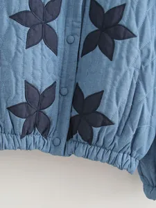 Dettaglio giacca in denim trapuntata con applicazioni floreali scure e bottoni