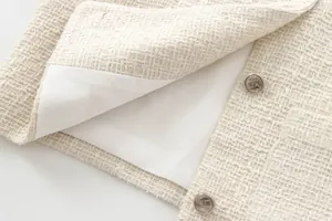 Detailed view of cream tweed jacket fabric, white lining and silver lion crest buttons