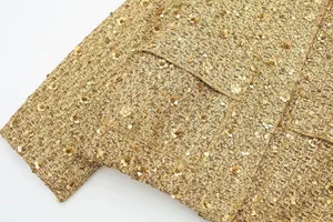 Detailansicht der goldenen Tweed-Textur und Pailletten auf einer schicken Damenjacke