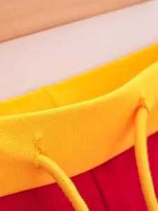 Gedetailleerde opname van de gele geribbelde tailleband en koord van rode shorts.