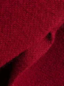 Makro-Detailaufnahme von rotem Strickmantelstoff zeigt weiche Textur und feine Fasern.