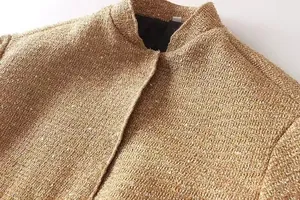 Detailaufnahme einer goldenen Pailletten-Tweed-Jacke mit Kragen und Stoffstruktur