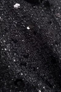 Detailansicht von schwarzem Tweed-Stoff mit funkelnden Pailletten auf einer Jacke