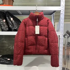 Detailansicht einer burgunderroten Steppjacke mit Zopfmuster auf weißem Regal.
