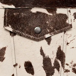 Detailopname van een jaszak met koeienprint, metalen drukknoop en strakke stiksels.