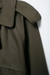 Detail shot of an olive green trench coat focusing on fabric texture and shoulder tabs