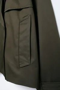 Macro detail of the reinforced welt pocket and fabric texture on olive green jacket