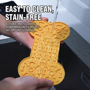 Bone-shaped yellow silicone pet slow feeder licking mat being rinsed under running water in a sink