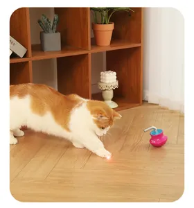 Ginger and white cat playing with an automatic laser tumbler toy on a wooden floor