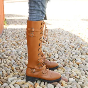 Detalle lateral de botas marrones altas con cordones y hebillas decorativas.