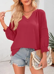 Modell mit roter V-Ausschnitt-Bluse mit eleganten Faltenärmeln und Häkeldetails.