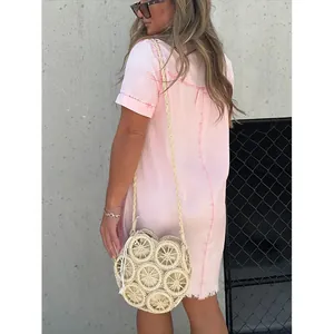 Détail d'une robe en jean rose avec ourlet effiloché et sac en paille tressée chic.