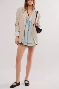 Vista completa de mujer con mono corto de mezclilla plisado sin mangas y blazer beige.