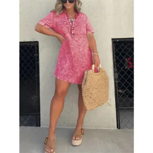 Détail d'une robe d'été en jean délavé rose avec col chemise et ourlet à franges.
