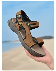 Vue détaillée de sandales d'été en cuir marron pour homme tenues devant une plage ensoleillée