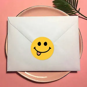 Gros plan d'un autocollant smiley jaune scellant une enveloppe blanche sur une assiette rose