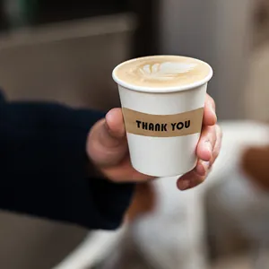 Détail d'un autocollant rond en papier kraft 'Thank You' scellant un gobelet blanc.