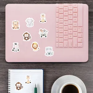 Niedliche Tieraufkleber dekorieren einen rosa Laptop und ein Notizbuch am Arbeitsplatz