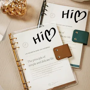 Gros plan détaillé des autocollants cœur 'Hi' noirs sur la couverture d'un carnet transparent.