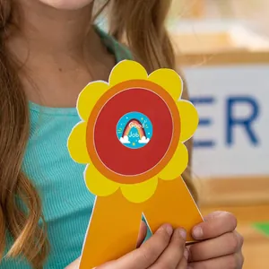 Detalle de un niño sosteniendo una cinta de premio en forma de flor con pegatina de arcoíris