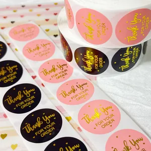 Close-up of pink and black Thank You stickers with elegant gold foil text for gift packaging.