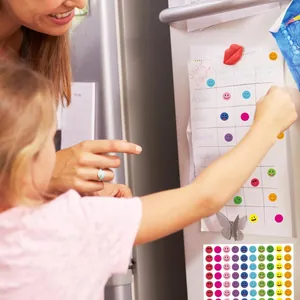 Detail of a child applying colorful smiley face reward stickers to a wall chore chart