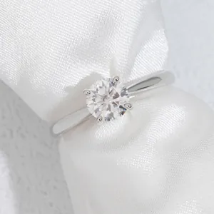 Primo piano di anello moissanite da 1ct con montatura a quattro griffe su raso bianco