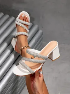 Close-up detail of white block heel sandals featuring sparkling rhinestone straps