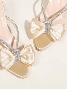 Primo piano di eleganti sandali in raso con fiocco e dettagli in strass lucenti.