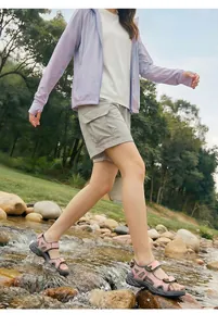 Pink outdoor sports sandals worn by a model walking through a shallow forest stream
