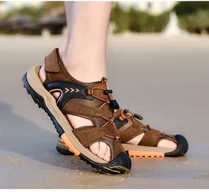 Side detail view of men's brown closed-toe beach sandals on a sandy beach background.