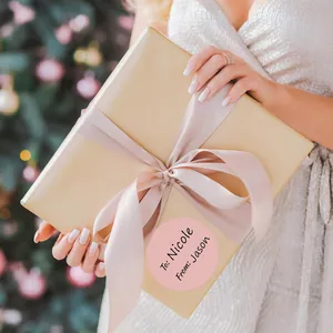 Primo piano di un'etichetta regalo circolare rosa su una scatola regalo incartata d'oro