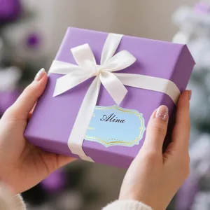 Close-up detail of a decorative gold foil gift tag sticker on a purple box held by hands