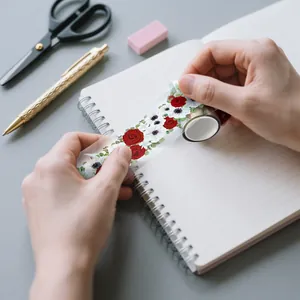 Close-up of hands applying decorative floral PET rose dream tape to a spiral notebook
