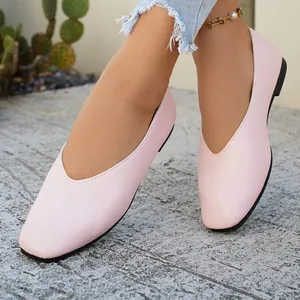 Close-up view of pink V-cut square toe leather flats worn on a sunny stone path