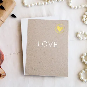Detailed close-up of a gold heart-shaped seal sticker on a textured minimalist kraft card